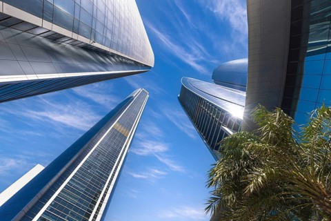 A dramatic low-angle view looking straight up at the modern glass Etihad Towers skyscrapers against