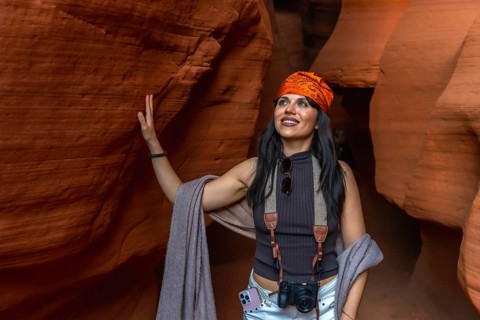 Woman standing inside antelope canyon, touching the textured sandstone wall while gazing upwards,