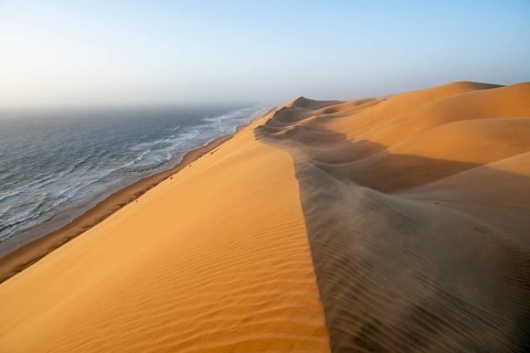 Sand dunes and sea in evening light, wind blowing sand across the dunes, view of the Atlantic coast