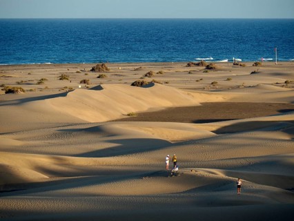 People walk across dunes on the beach in the light of the evening sun, Maspalomas Dunes, Gran