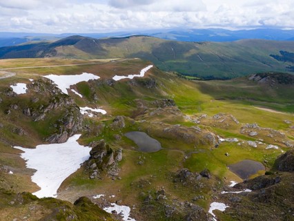A mountainous landscape with snow and green areas under a cloudy sky, aerial view, Transalpina High
