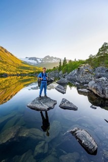 Young man standing on a rock in water, enjoying the landscape, picturesque mountain scenery in the