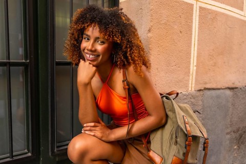 Young woman with beautiful afro hair smiling cheerfully, posing in a vibrant orange top and a