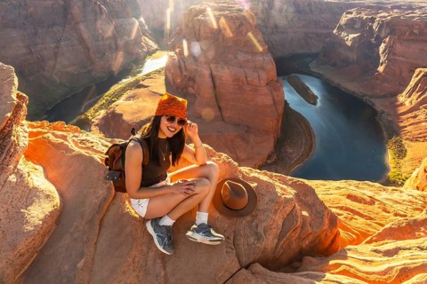 Young woman smiling while sitting on a cliff edge overlooking the winding colorado river at
