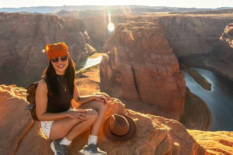 Young woman smiling while sitting on a cliff edge, overlooking the colorado river winding through