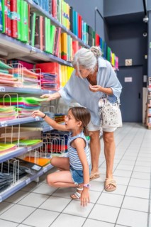 Grandmother and granddaughter choosing colorful folders and binders from a retail store shelf,