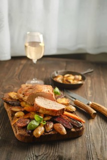 Dinner features roasted meat and vegetables served on a wooden board. A glass of white wine is