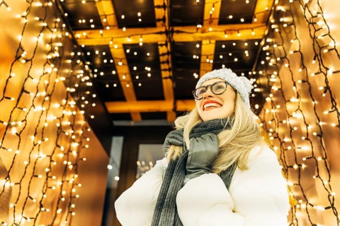 Young woman in winter clothing looking up under festive lights. A person in a white winter coat,