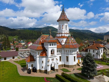 Orthodox church with decorative roof in a mountainous landscape under blue sky with clouds, aerial