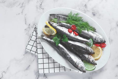 Fresh Herring fish, ready to cook, with herbs and spices, on a white platter, in the kitchen