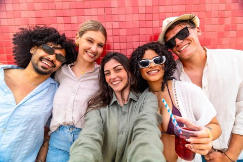 Diverse group of young friends is smiling and happily posing for a close up selfie outdoors against