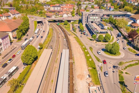 Aerial view of railway tracks in a city with surrounding roads, vehicles and buildings in sunshine,