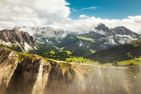 Aerial panorama tourist walk hike Seceda ridge with Odle peaks rise over clouds with steep