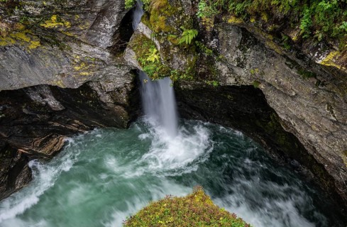 View of a small waterfall and a pool from the historic Øvstestølbrua stone arch bridge, long