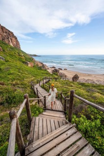 Young pretty woman wearing dress off coast and sea at Robberg Nature Reserve, Plettenberg Bay,