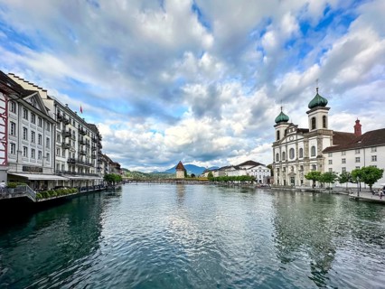 Elegant building and church with turquoise domes along the Reuss under cloudy sky, Lucerne,