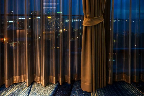 Hotel room view through curtain illuminated city scenery, Pattaya, Thailand