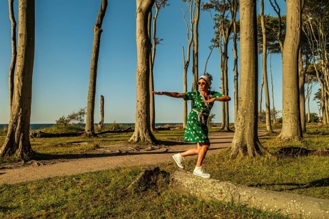 A woman (54) in a green tennis dress and white trainers is surfing on a tree, Ghost Forest,