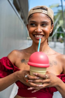 Young woman smiling while holding a colorful frozen slushy drink on a sunny day, showcasing a