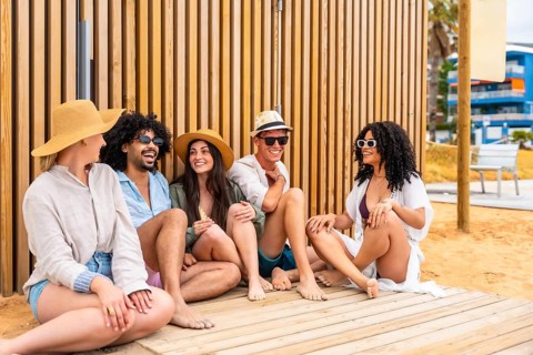 Group of diverse friends wearing casual summer clothing and sunglasses, sitting on a wooden