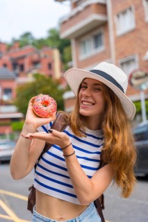 Young smiling woman wearing a hat and striped t shirt, holding a colorful pink donut with