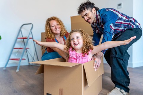 Happy family unpacking in their new home, parents pushing their smiling daughter doing airplane