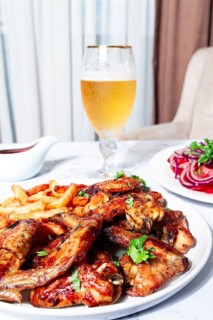 Delicious barbecue chicken wings, with French fries, salad and a refreshing drink, at a cozy table,