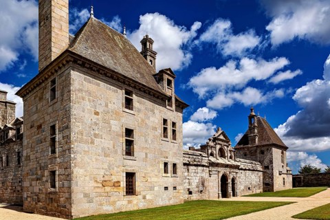 Historic stone buildings under a light blue sky with few clouds, Château de Kerjean Castle in