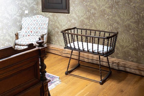 A vintage style room features a dark wooden baby cradle with spindled sides and a white mattress.