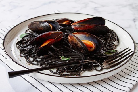 Black spaghetti with mussels, on a white plate with a fork, on a striped napkin, marble background,