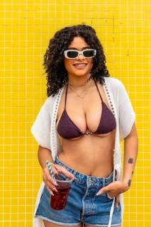 Young woman smiling while holding a refreshing cold drink, dressed in a bikini top and denim