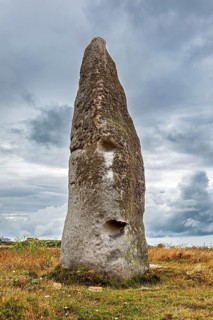A massive menhir stands in a meadow under a cloudy sky. A monumental impression of the Stone Age,