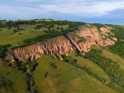 Landscape with rocky slopes and grassy areas surrounded by green vegetation under a clear sky,