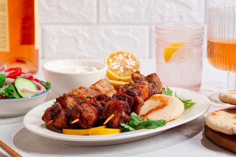Souvlaki, a Greek dish, grilled meat shish kebab, on a plate with flatbreads, and lemon slices,