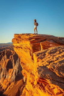 Woman stands on a canyon cliff edge at horseshoe bend, gazing over the vast arizona desert during