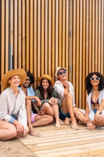 Diverse group of young adults barefoot on a wooden boardwalk, laughing and relaxing together in