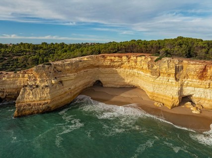 Drone view of cliffs above Benagil Cave in Algarve, Portugal, with a sandy cove, limestone rock