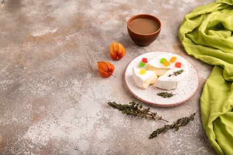 White Camembert mold cheese on brown concrete background and green textile, cup of coffee, side