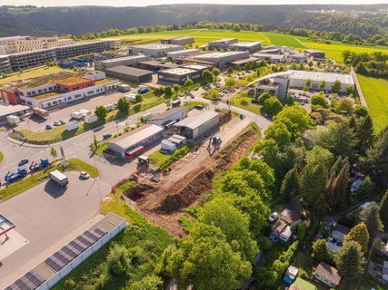 An aerial view of a construction site in an industrial area with surrounding green trees and sunny