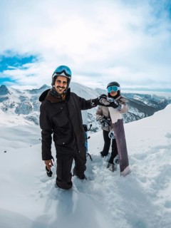 Happy couple on an alpine peak holding snowboards and fist bumping, smiling under a bright blue sky