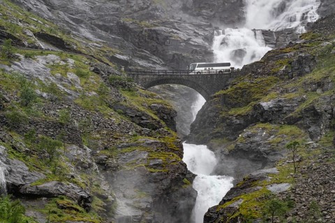 Coach on a bridge in front of heavily swollen Stigfossen waterfall, Trollstigen, near Åndalsnes or