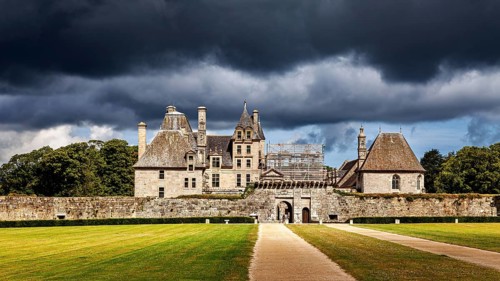 A castle with green lawns and dark skies bathed in dramatic light, The Château de Kerjean Castle in