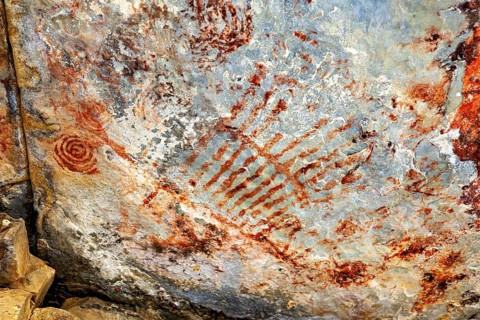 Red line patterns and handprints on a rock surface, prehistoric rock carvings in the thorny savanna