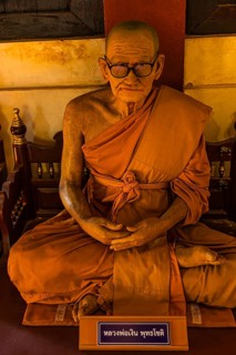 Wax figure of a seated Buddhist monk wearing glasses in orange robe, Wat Phra Singh Buddhist temple