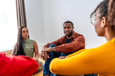 Diverse individuals sitting on the floor, actively listening and engaging in a therapy or support