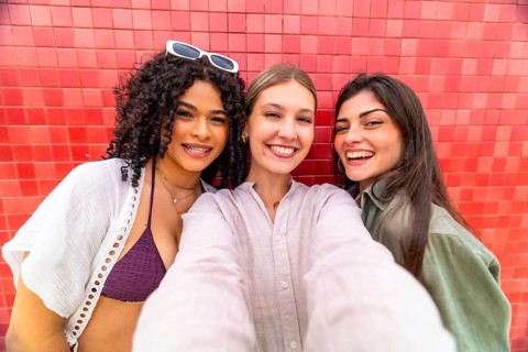 Diverse young women friends taking a happy selfie together, smiling brightly at the camera while