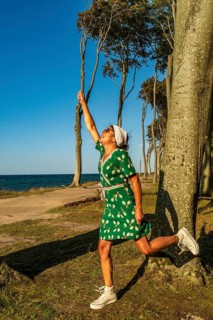 A woman (54) wearing a green tennis dress and white trainers returns an imaginary ball,