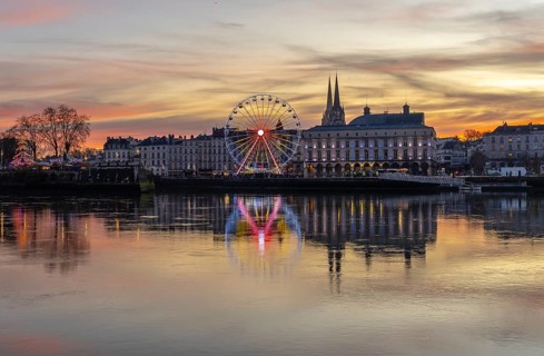 Bayonne, france ferris wheel sparkling with lights reflecting in the adour river water, showcasing