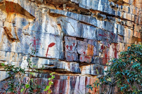Red symbols and figures on a rock wall in natural surroundings, prehistoric rock carvings in the