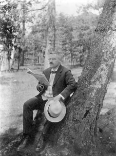 Man sitting on a tree stump next to a birch tree and reading newspaper in the forest, relaxation,